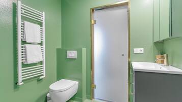 A bathroom with a white toilet, a towel rack with two towels, a sink with a faucet, and a door with a gold frame.