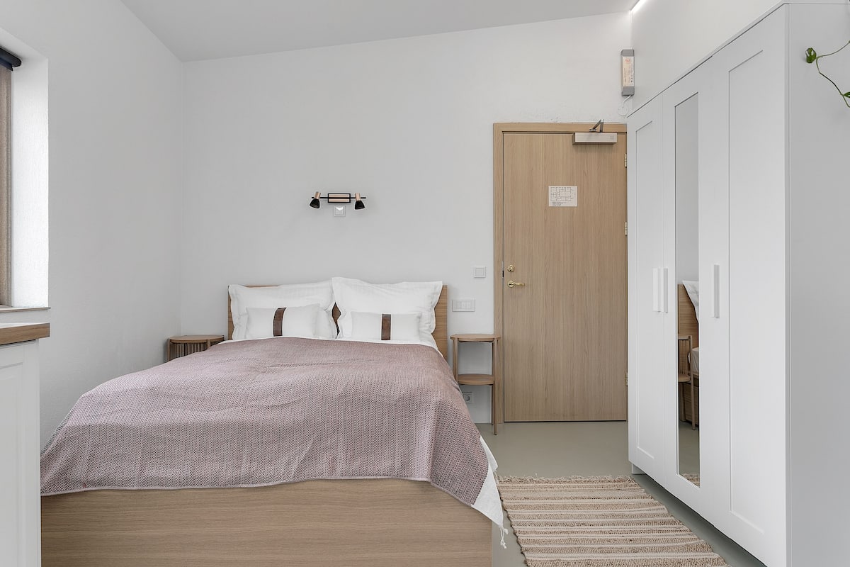 A bedroom with a bed, a wooden wardrobe, a bedside table, and a nightstand.