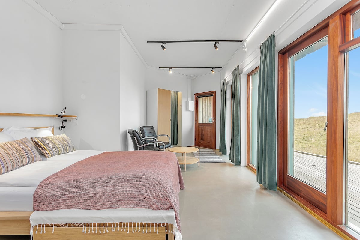 A modern hotel room with a large bed, a desk, a chair, and a view of the outdoors.