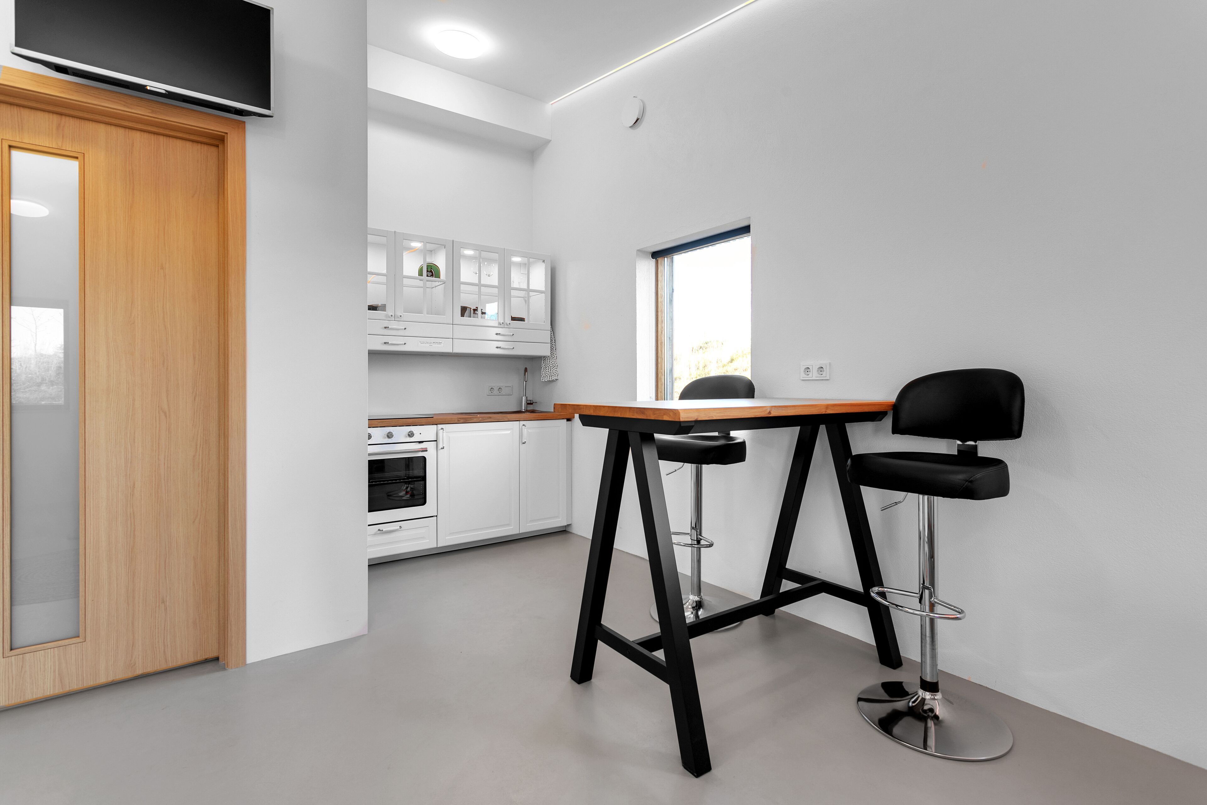 A modern kitchen with white cabinets, a wooden door, and a black bar stool.