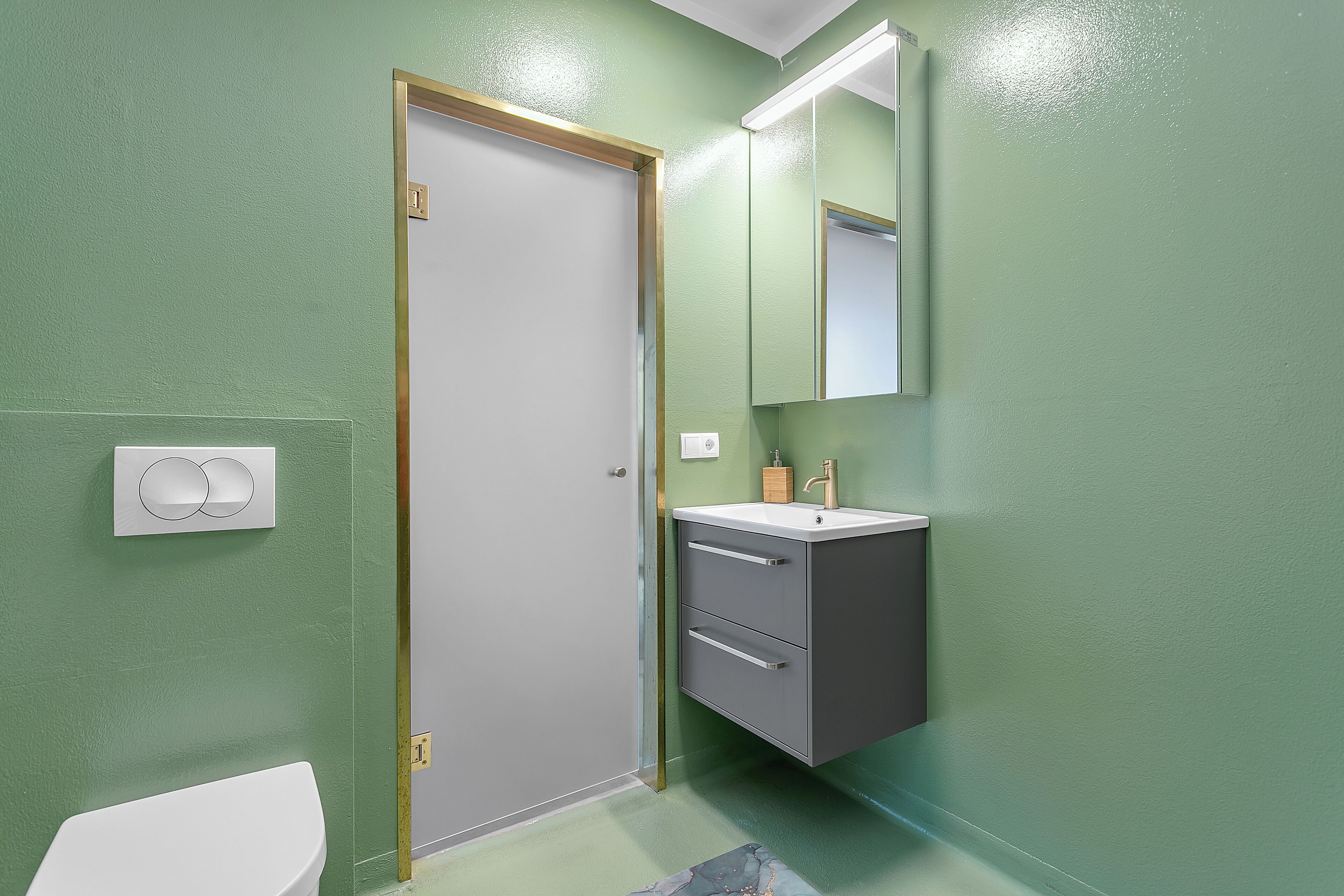 Een badkamer met een wit toilet, een wastafel met een spiegel erboven en een deur met gouden lijst.