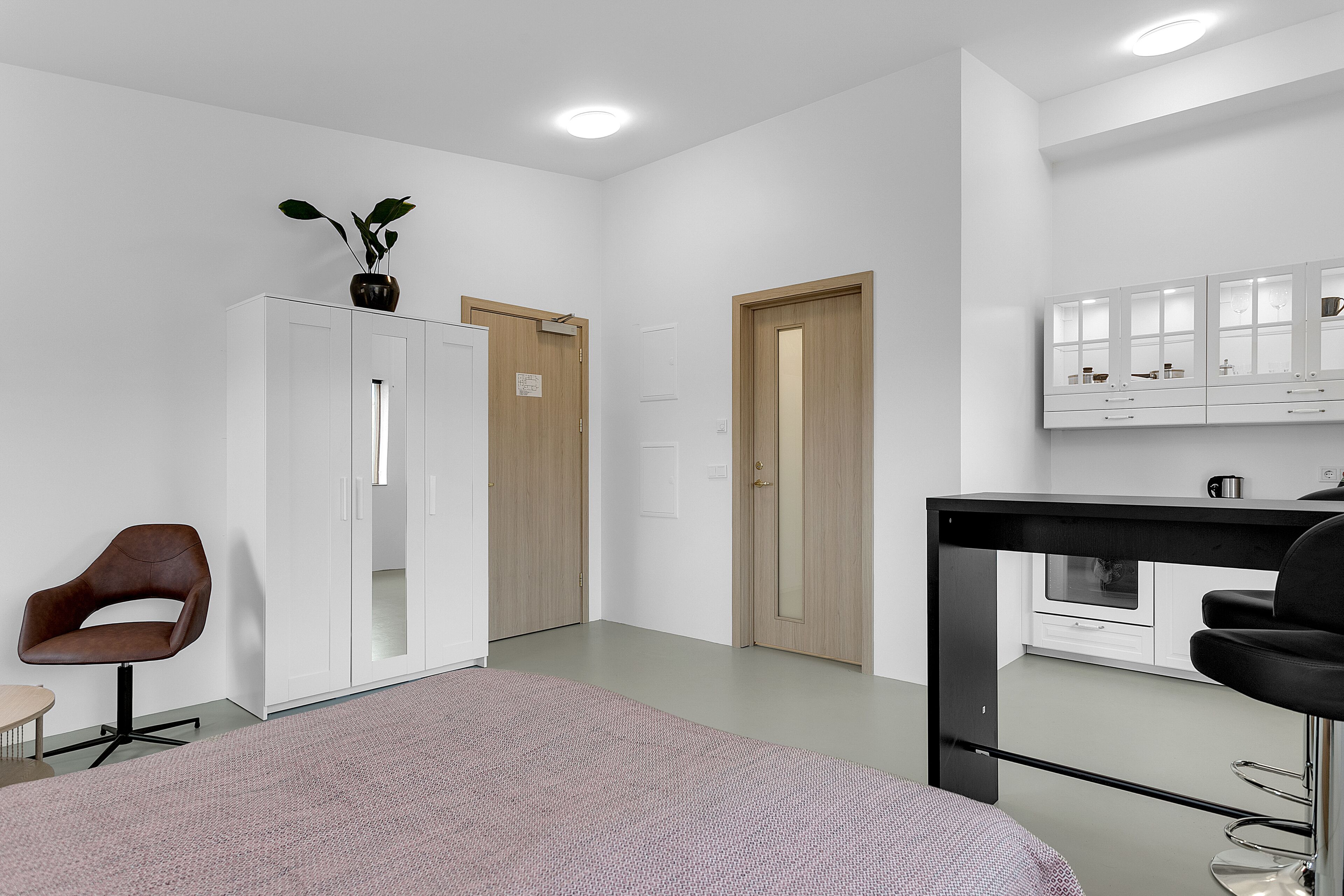 A modern room with a large bed, a desk with a chair, a wardrobe, and a mirror.