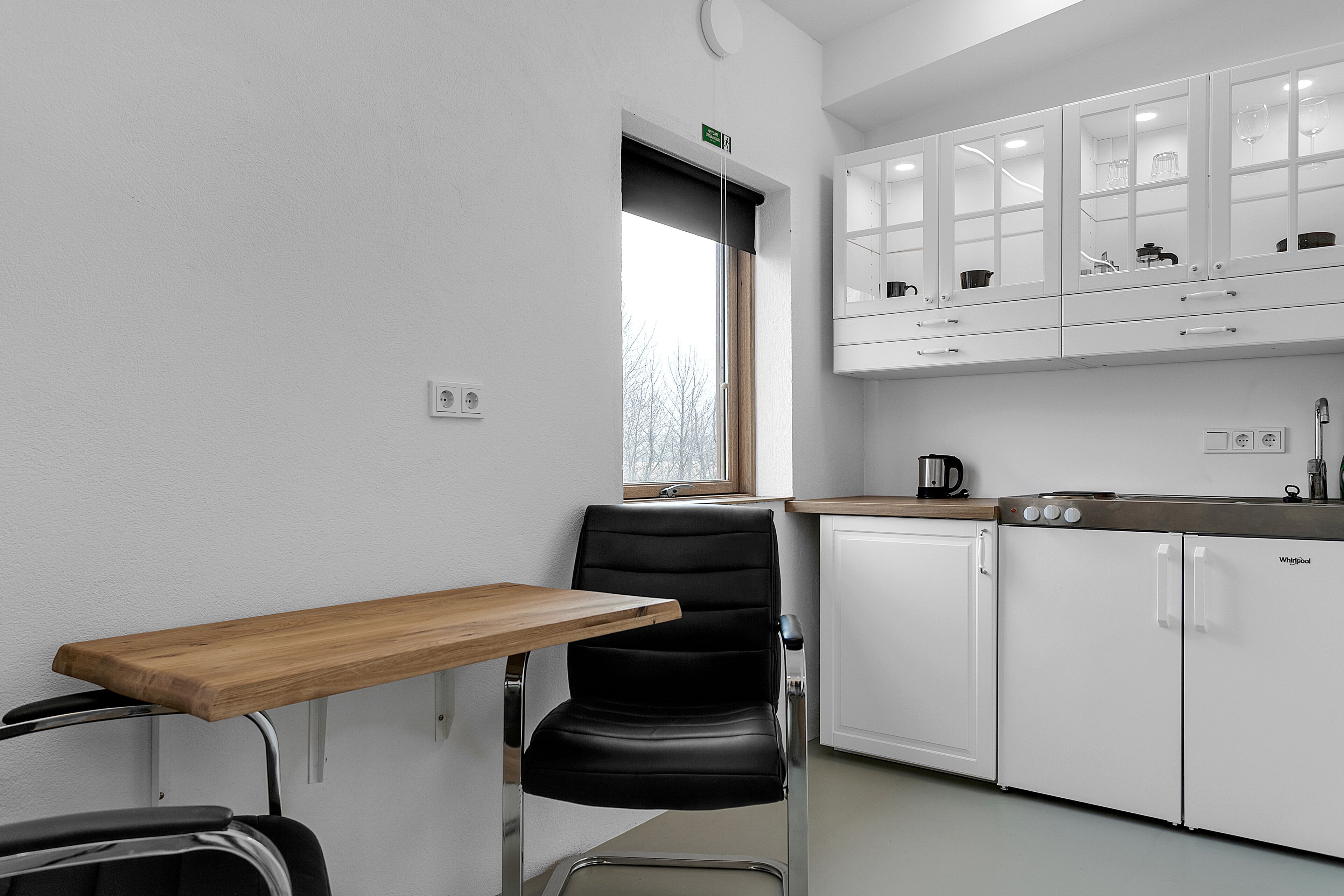 Una cocina compacta con una silla negra, una mesa de madera y armarios blancos.