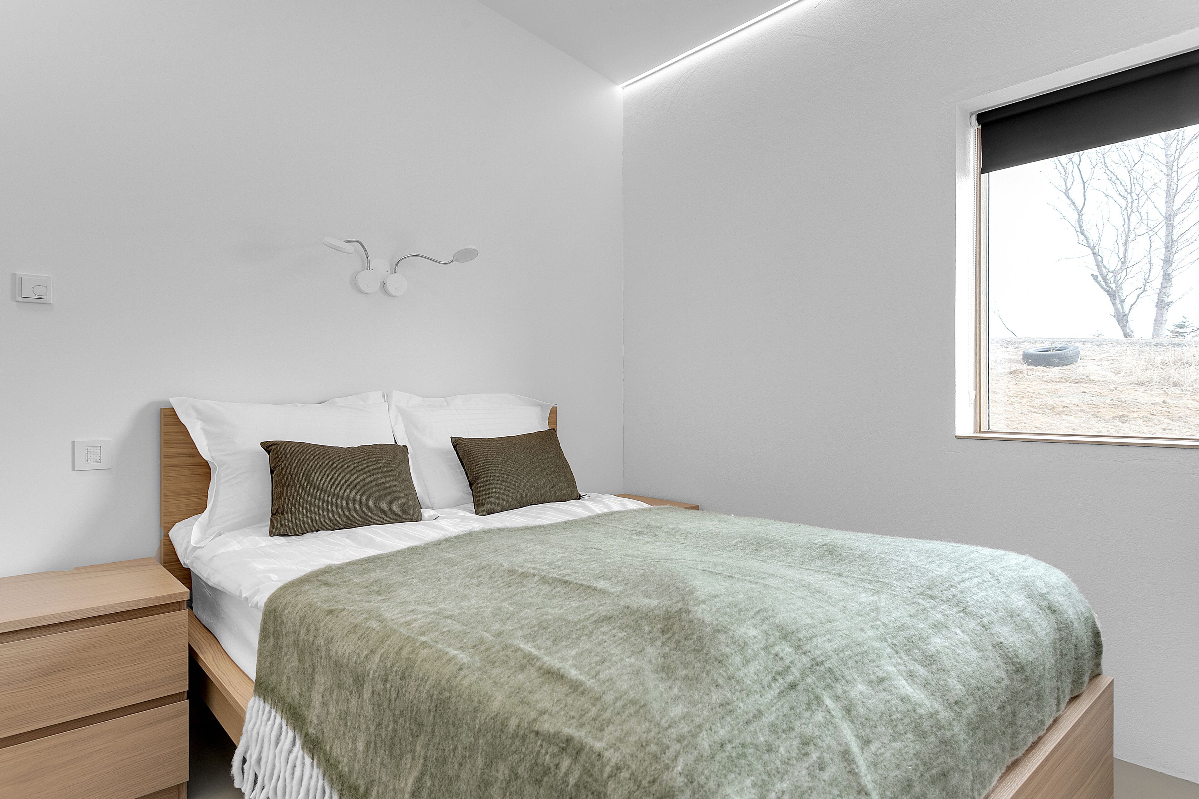 Een moderne slaapkamer met een bed, nachtkastjes en een raam met uitzicht op bomen.