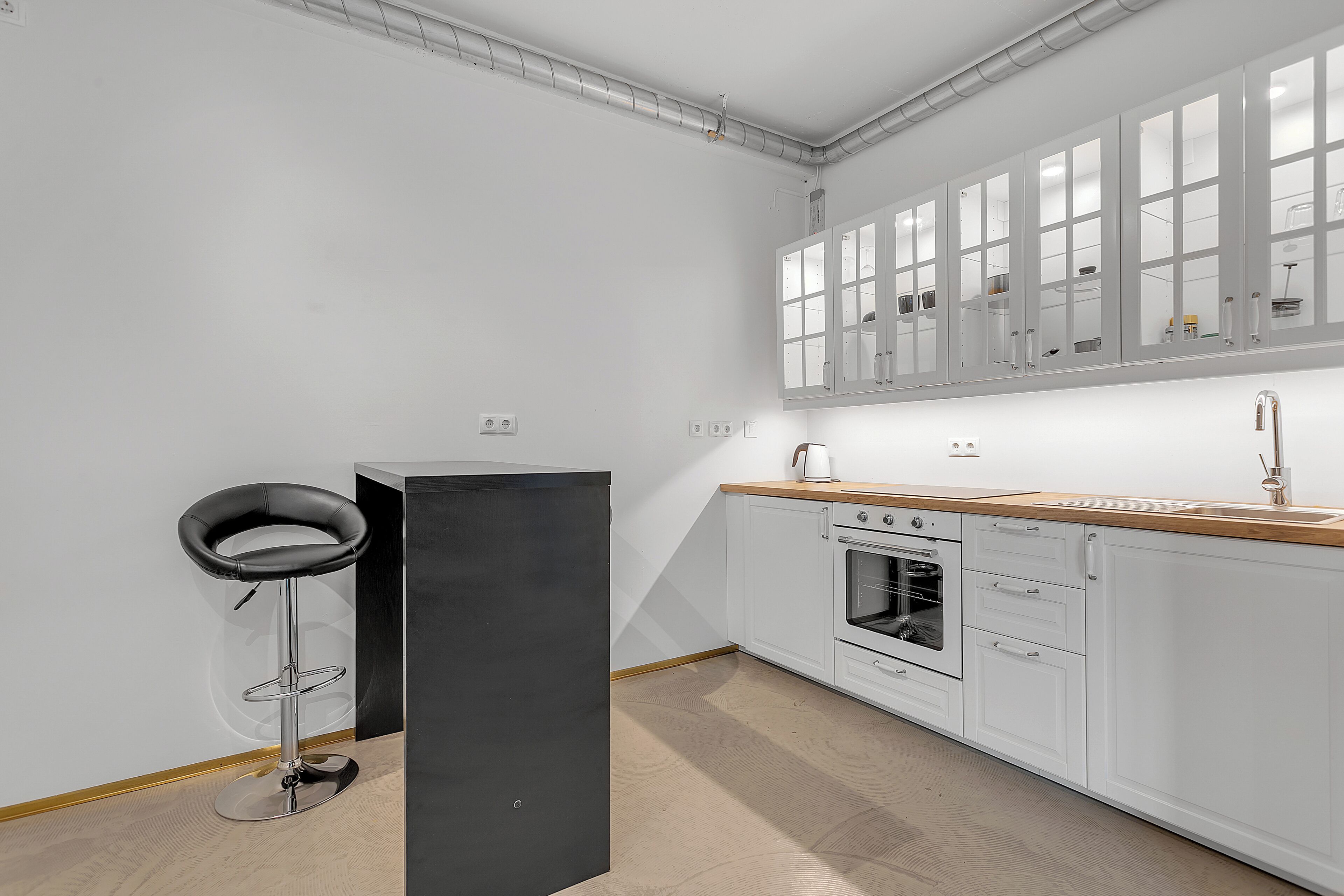 Una cocina moderna con armarios blancos, una encimera de madera y un taburete negro.