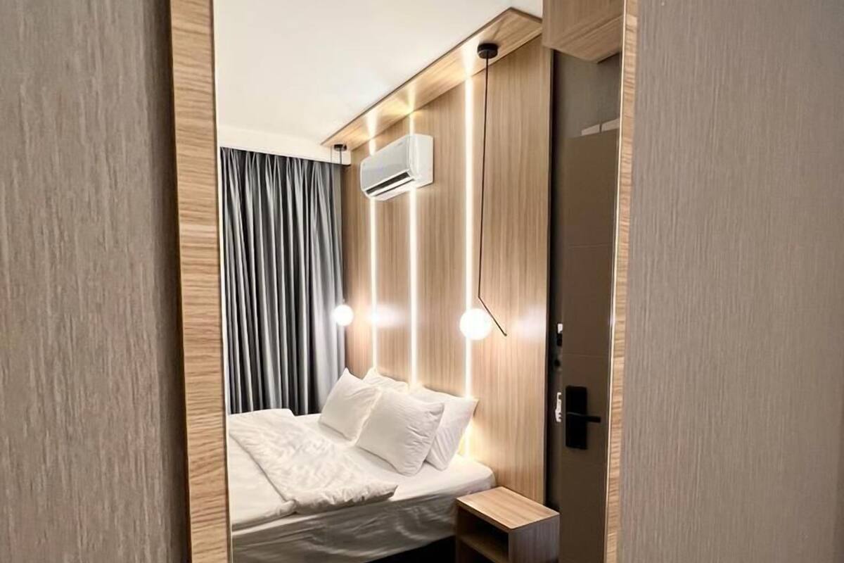 Een moderne hotelkamer met een net opgemaakt bed, een klein nachtkastje, een wandairconditioner en een deur met een handvat.