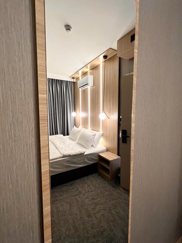 A modern hotel room with a neatly made bed, a small bedside table, a wall-mounted air conditioner, and a door with a handle.
