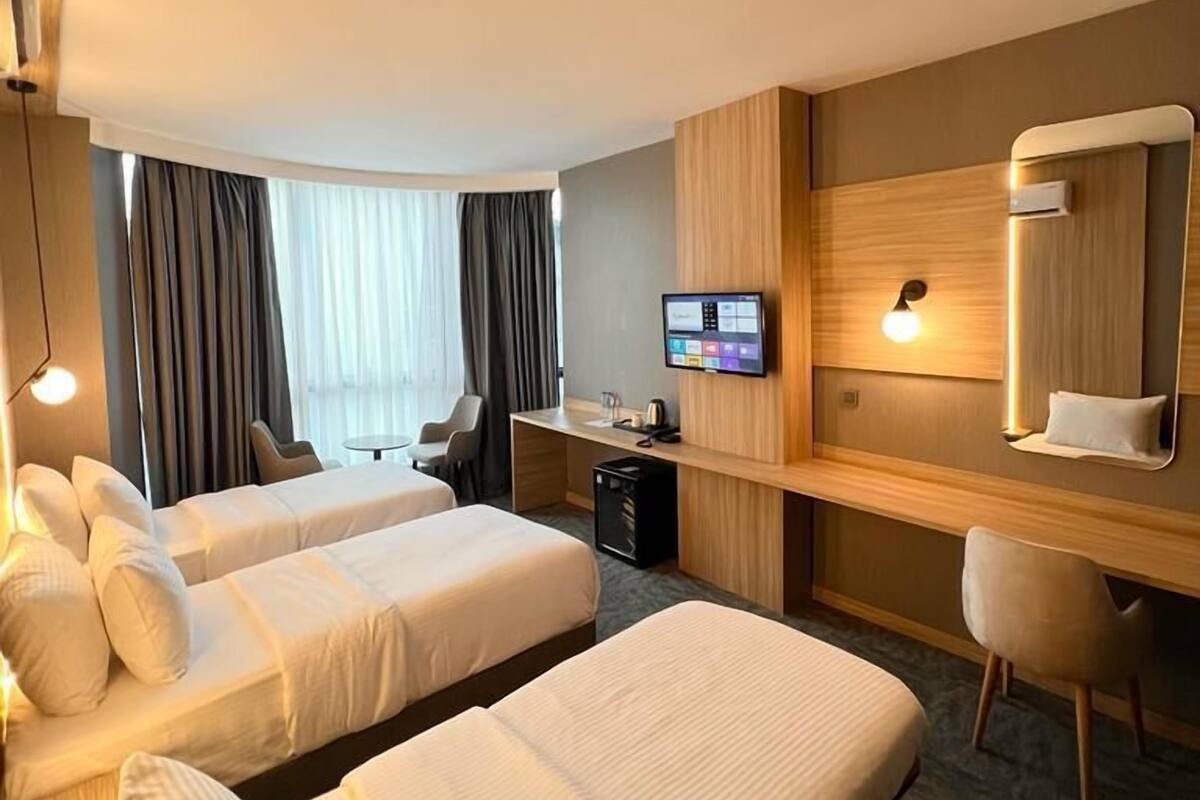 Een hotelkamer met twee éénpersoonsbedden, een bureau met een computer, een stoel en een grote spiegel.