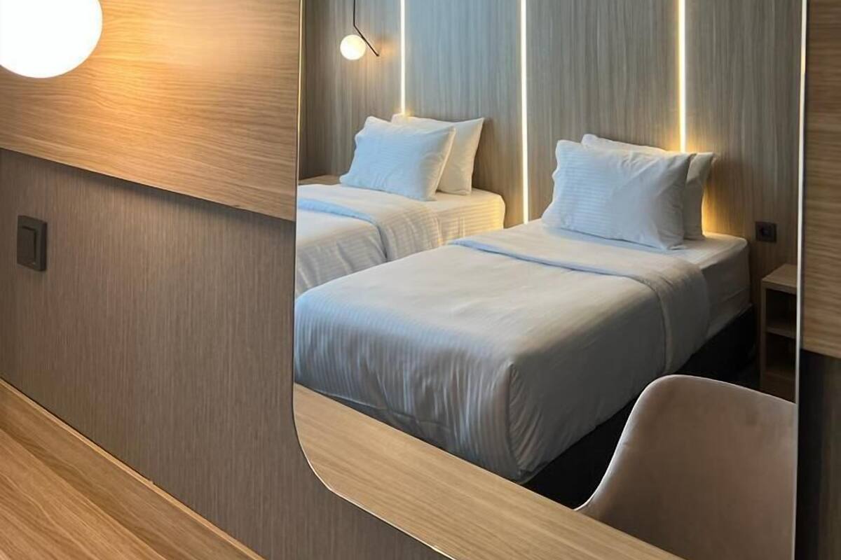 Een moderne hotelkamer met een grote spiegel die twee bedden, een wandairconditioner en een vloerlamp weerspiegelt.