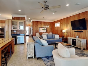 A modern living room with a sofa, a coffee table, a TV, and a kitchen area with wooden paneling.