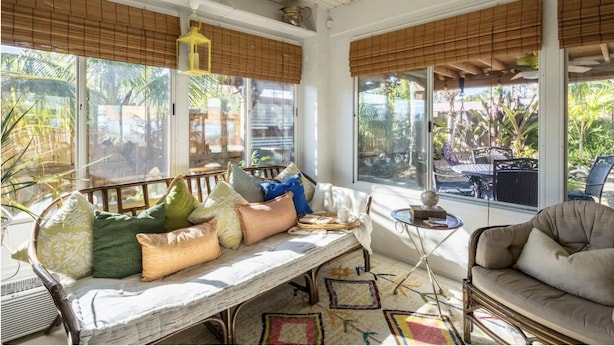 A sunlit room with a wooden bench, cushioned seating, and large windows overlooking a garden.