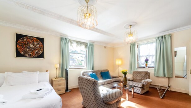 A hotel room with a bed, a sofa, two armchairs, a small table with a vase, and two windows with curtains. - Remarkable 3-bed Apartment in London (London)
