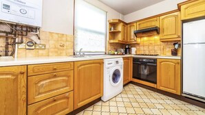 A compact kitchen with wooden cabinets, a washing machine, a stove, and a refrigerator. - Remarkable 3-bed Apartment in London (London)