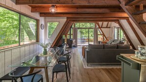 Un loft espacioso con un techo alto, vigas de madera, una zona de comedor con mesa de vidrio y un rincón de descanso acogedor con sofá y cojines.