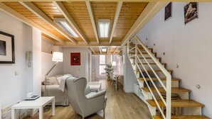 A modern interior with a wooden staircase, a living area with a sofa and table, and a dining area with chairs. - Waou Chamberi VII - Alquiler Corta Duración (Madrid)