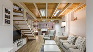 A modern living room with a wooden ceiling, a staircase, a sofa, a coffee table, and a TV. - Waou Chamberi VII - Alquiler Corta Duración (Madrid)