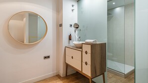 A modern bathroom with a round mirror, a vessel sink, and a glass shower enclosure. - Waou Chamberi VII - Alquiler Corta Duración (Madrid)