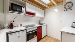 A modern kitchen with white cabinetry, a built-in microwave, a red dishwasher, and a small refrigerator. - Waou Chamberi VII - Alquiler Corta Duración (Madrid)