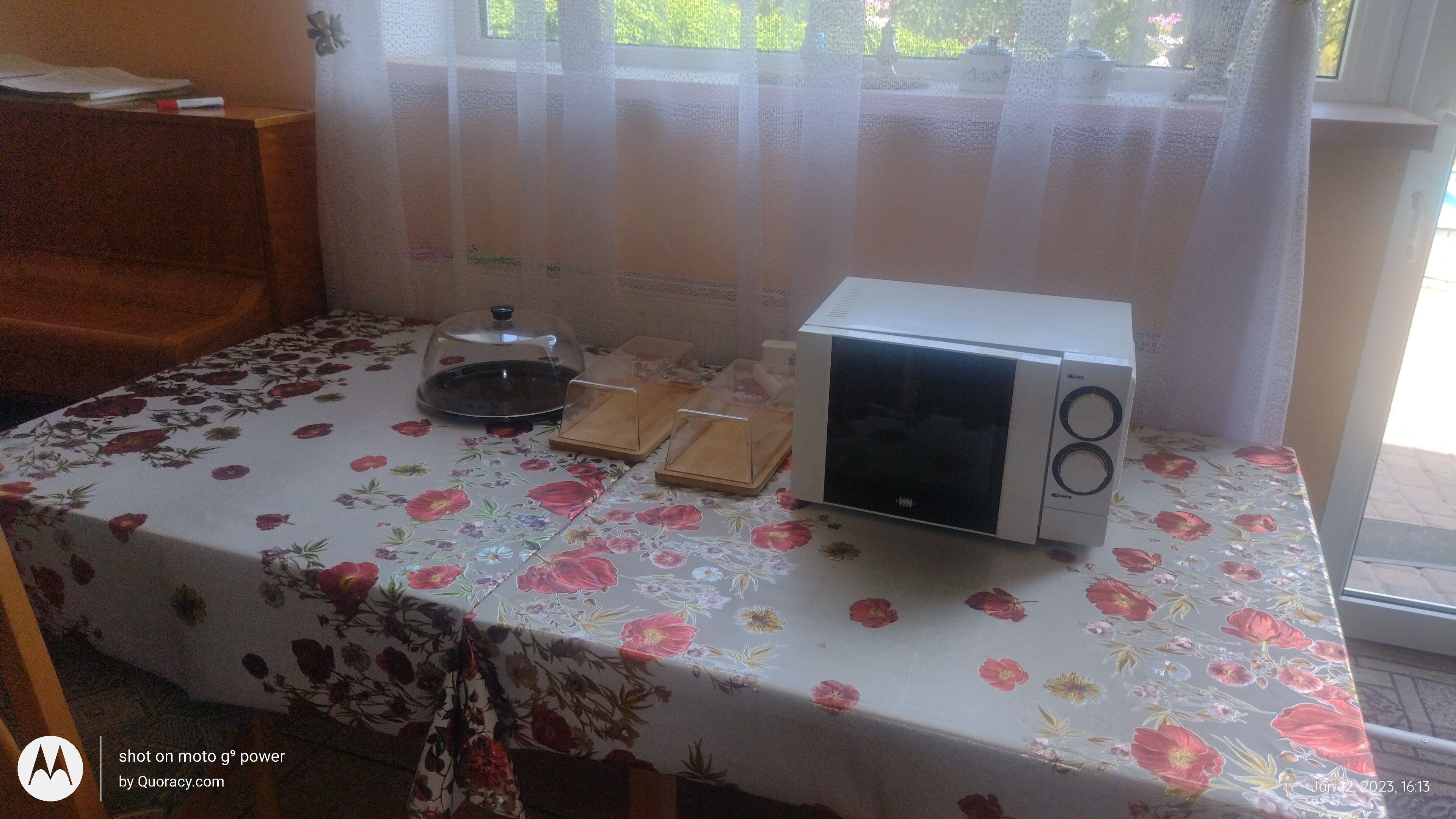 Keittiössä on pöydällä kukkakuviollinen pöytäliina, mikroaaltouuni, vedenkeitin ja teekannu.
