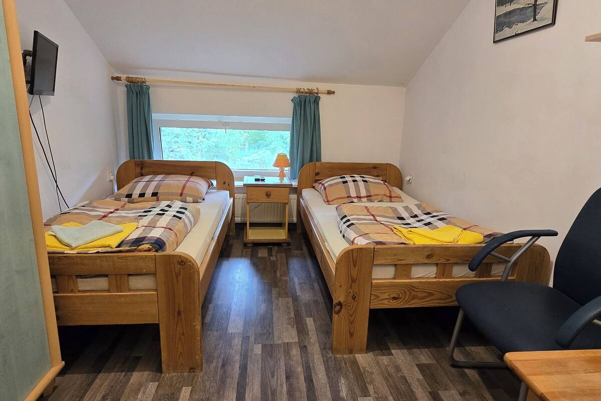 Een kleine kamer met twee houten bedden, een bureau, een stoel en een raam met gordijnen.