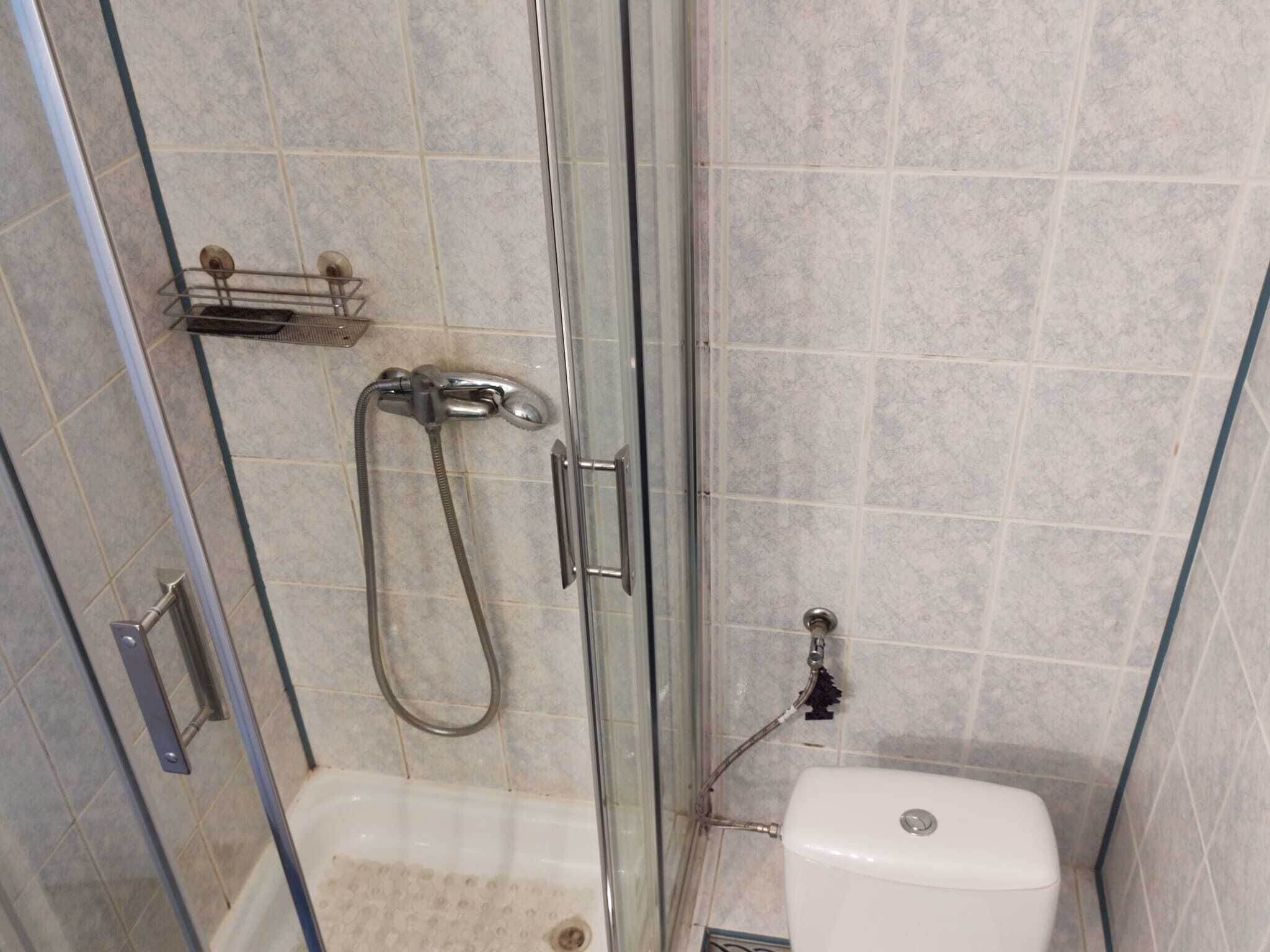 A glass-enclosed shower stall with a handheld showerhead and a wall-mounted faucet.