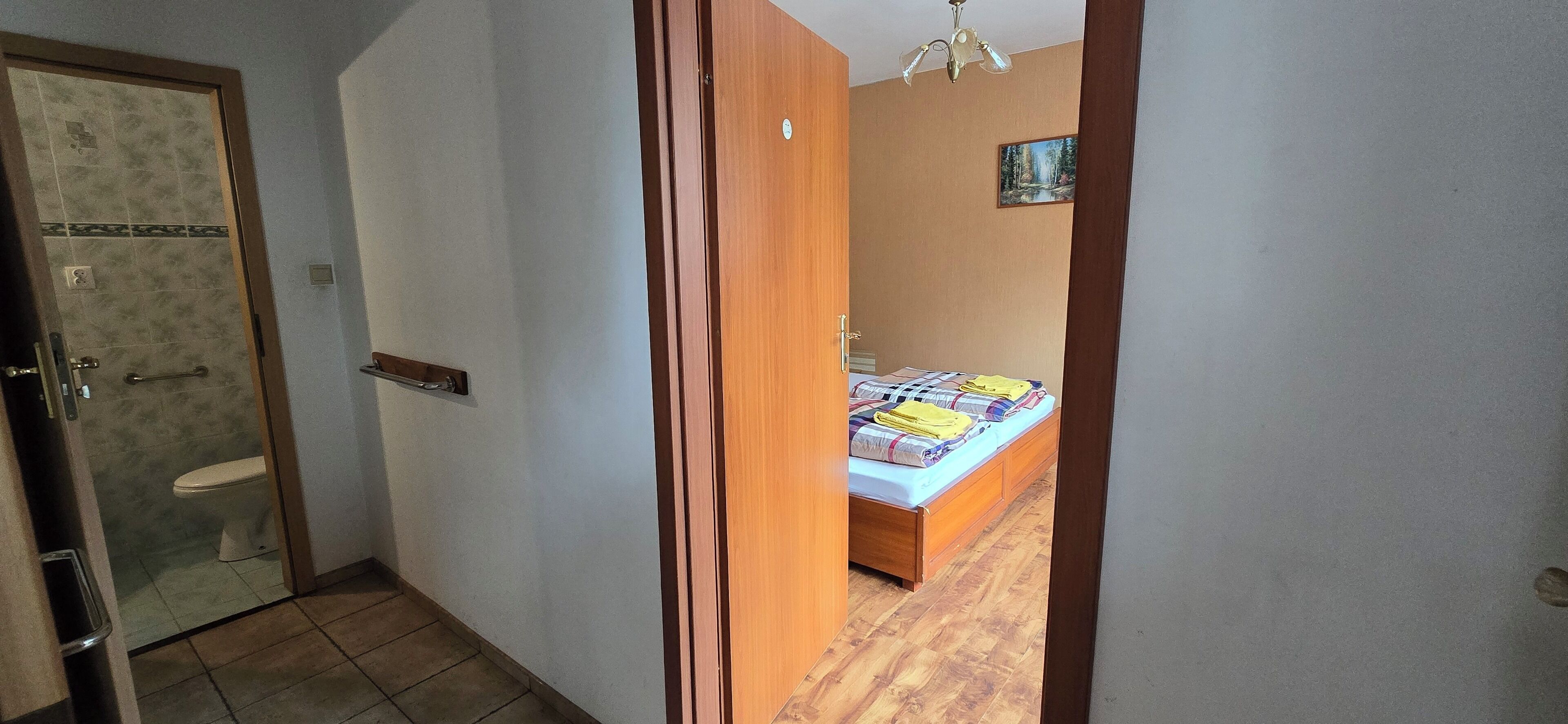Um corredor estreito com uma porta de madeira que dá para um banheiro e um quarto.