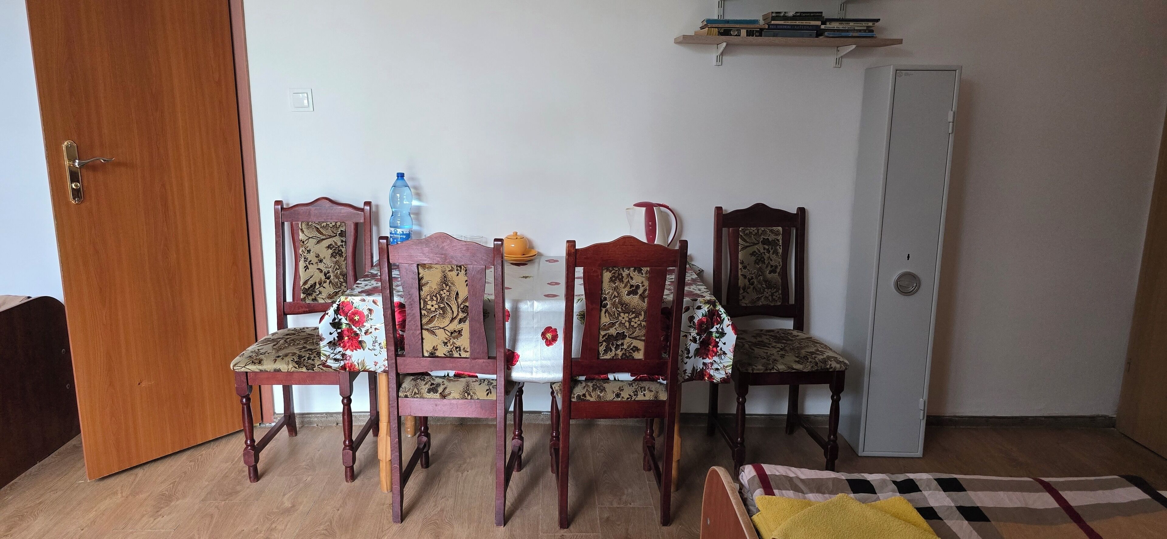 Un comedor con una mesa de madera y cuatro sillas, una botella de agua y un hervidor sobre la mesa.