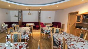 Un espace repas comprenant plusieurs tables et chaises, une horloge au mur et un buffet en bois contenant de la verrerie.