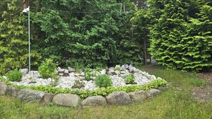 Un jardin avec une bordure circulaire en pierres, diverses plantes et une clôture en bois.