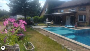 Un jardin à l’arrière d’une maison, avec une piscine, une terrasse dotée de mobilier d’extérieur et une maison en briques.