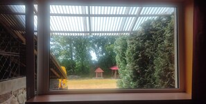 Blick durch ein Fenster mit einer Metallverkleidung, ein gelbes Fahrzeug und ein Gebäude mit rotem Dach auf einer grünen Fläche.