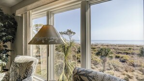 Ein Zimmer mit großen Fenstern und Blick auf eine Küstenlandschaft, eine Stehlampe und gestreifte Sessel.
