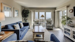 Ein Wohnzimmer mit blauem Sofa, einem Couchtisch und Meerblick durch große Fenster.