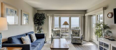 A living room with a blue sofa, a coffee table, and a view of the ocean through large windows.