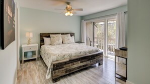 A bedroom with a wooden bed, a nightstand, a ceiling fan, and a view of the outdoors through a sliding door. - Sunset Rentals | Continental Club 16 (Hilton Head Island)