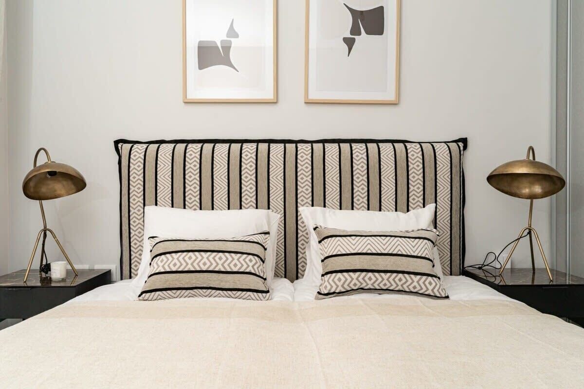 A neatly made bed with striped bedding, two bedside lamps, and two framed abstract artworks on the wall.