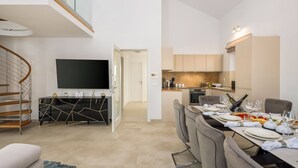 A modern apartment with a dining area, kitchen, and a living room with a TV.