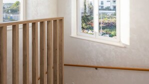 A staircase with a wooden handrail and a view of a building through a window.
