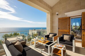 A balcony with a view of the sea, furnished with sofas, tables, and a glass railing.
