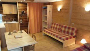 A cozy cabin interior with a wooden dining table, a sofa, and a small kitchen area. - 10m from resort center, 2nd floor, balcony, tv, ski locker, 28m², Tignes (Tignes)