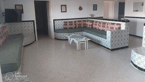 A living room with a curved sofa, a small table, and a kitchen area in the background.