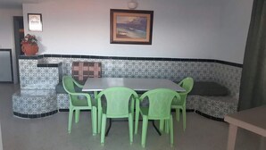 A dining area with a white table and green chairs, a patterned bench, and a framed picture on the wall.