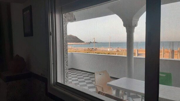A room with a large window overlooking a beach, a checkered floor, and a table with chairs.