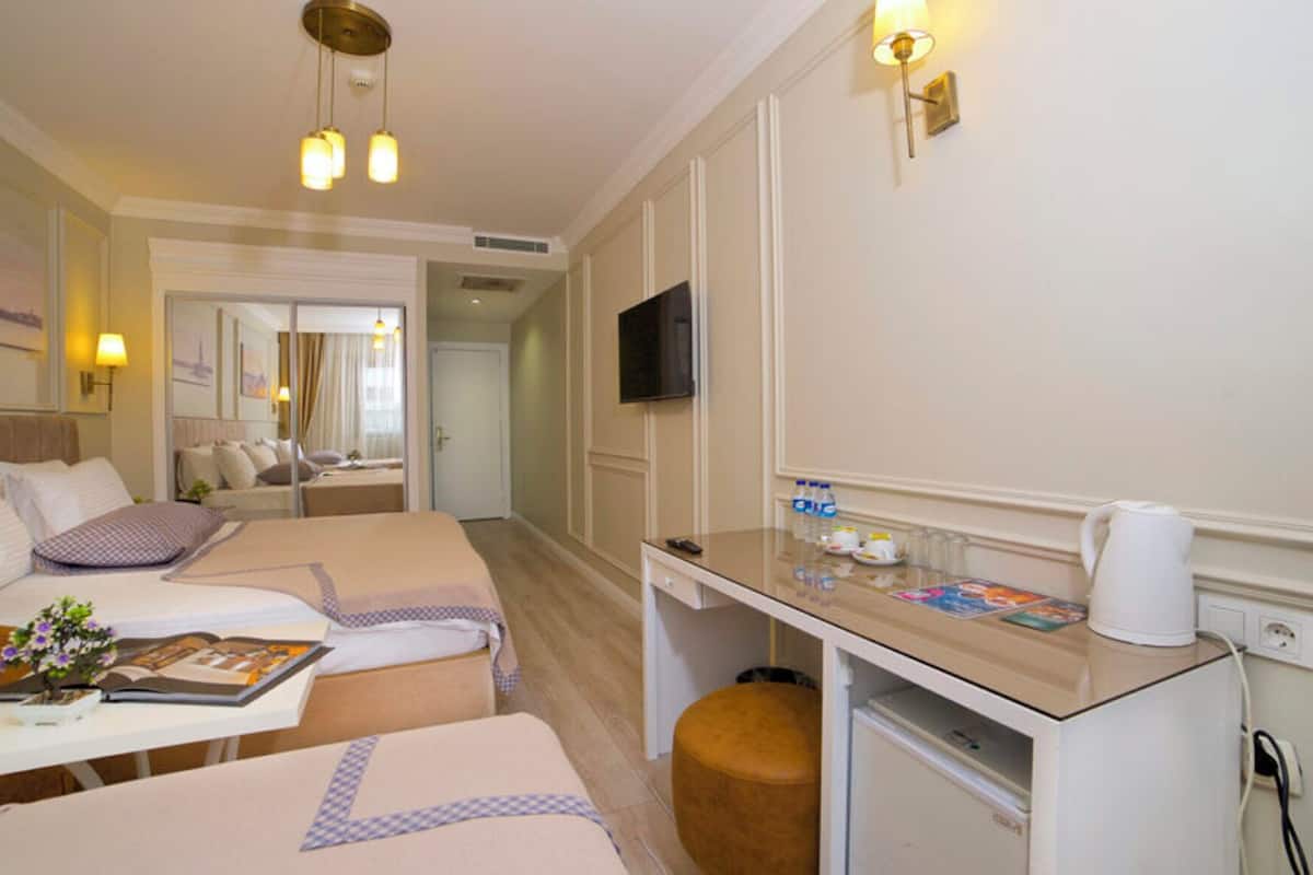 Une chambre d’hôtel avec deux lits, un bureau avec un ordinateur, une télévision et un petit réfrigérateur.
