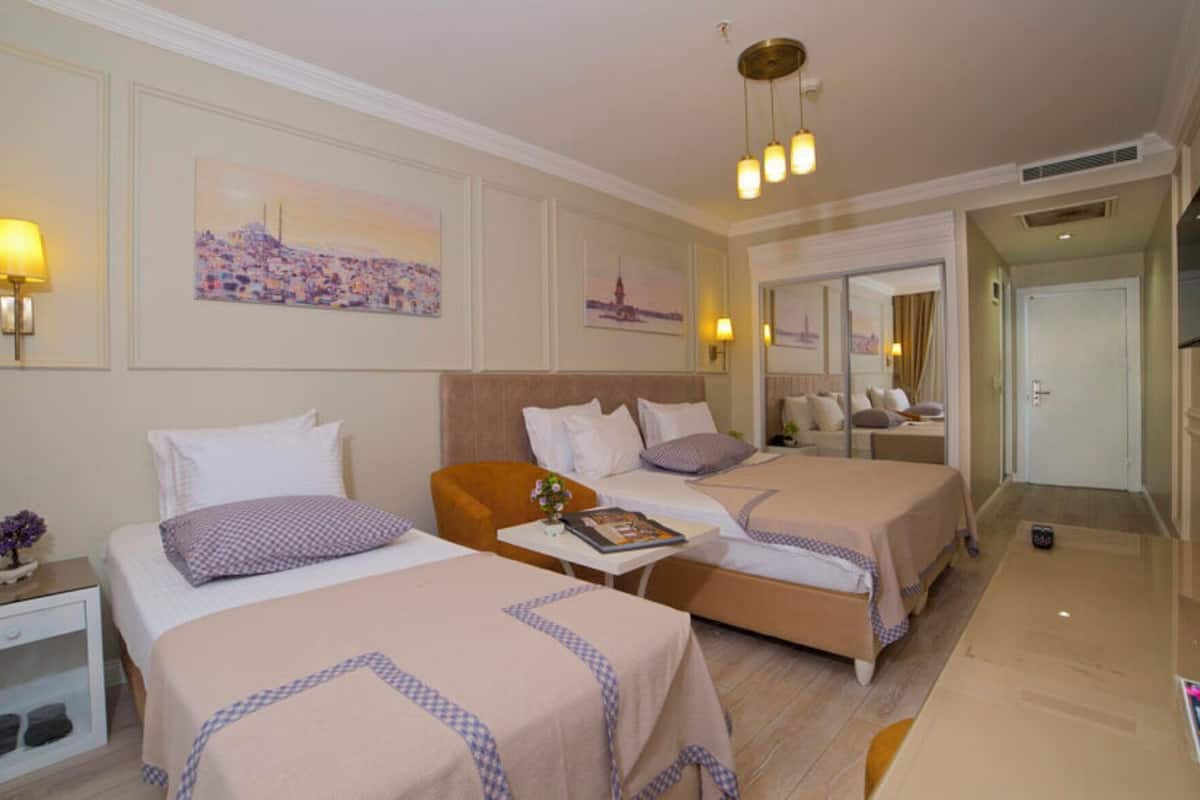 Une chambre d’hôtel avec deux lits, une petite table, une table de chevet, un miroir et un téléviseur.