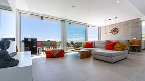 Ein modernes Wohnzimmer mit Sofa, Hocker und Couchtisch, großen Fenstern mit Aussicht und einer Statue auf einem Tisch.
