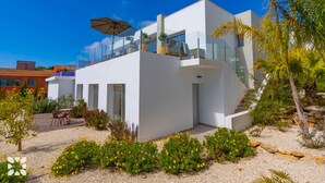 Ein modernes, zweistöckiges Haus mit weißer Fassade, einem Balkon und einer Treppe, die zum oberen Stockwerk führt.