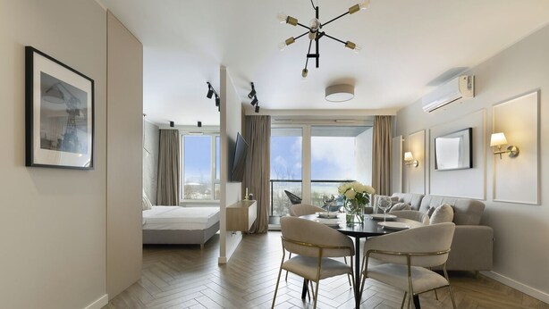 A modern hotel room with a dining area, a sofa, a TV, and a large window offering a city view. - Elite Apartments Stępkarska Premium (Gdansk)
