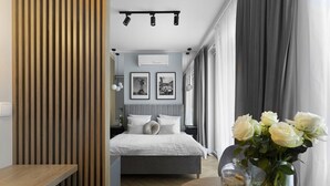 A modern bedroom with a bed, a wooden slat wall, a bedside table, a vase with flowers, and a view of another room with a bed and curtains. - Elite Apartments Stępkarska Premium (Gdansk)