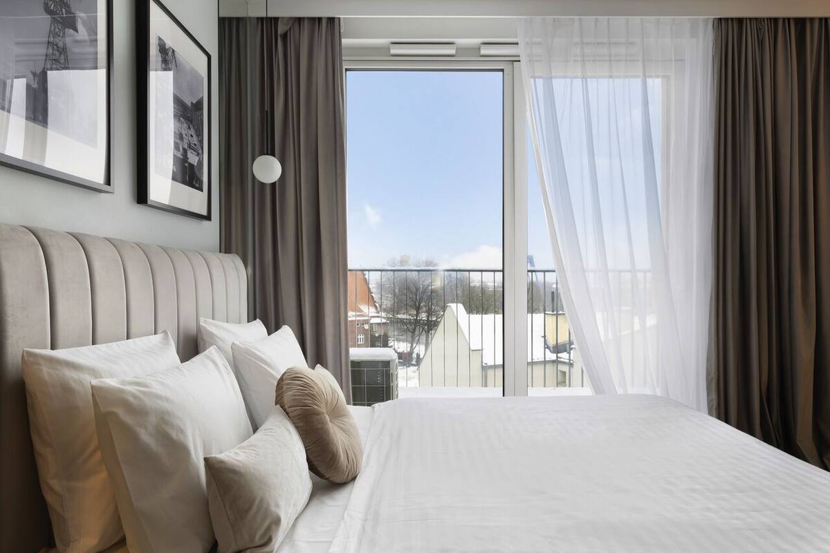 Un cuarto de hotel con una cama grande, vistas de la ciudad desde un balcón y cuadros en la pared.